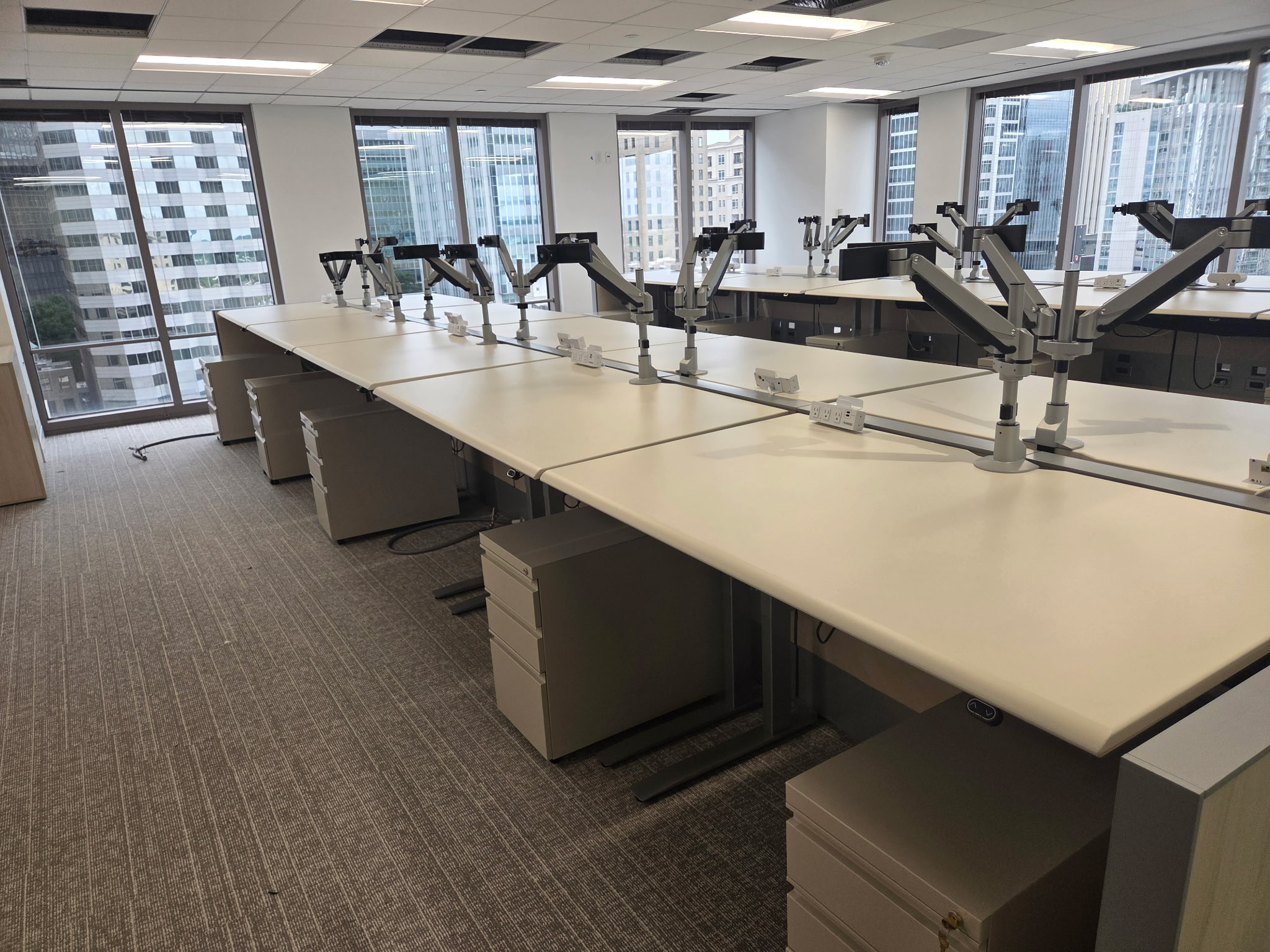 Shared benching workstations with monitor arms beside office windows